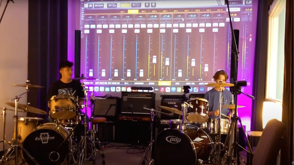 Music students Carter and Livy playing drums with mixing software displayed behind